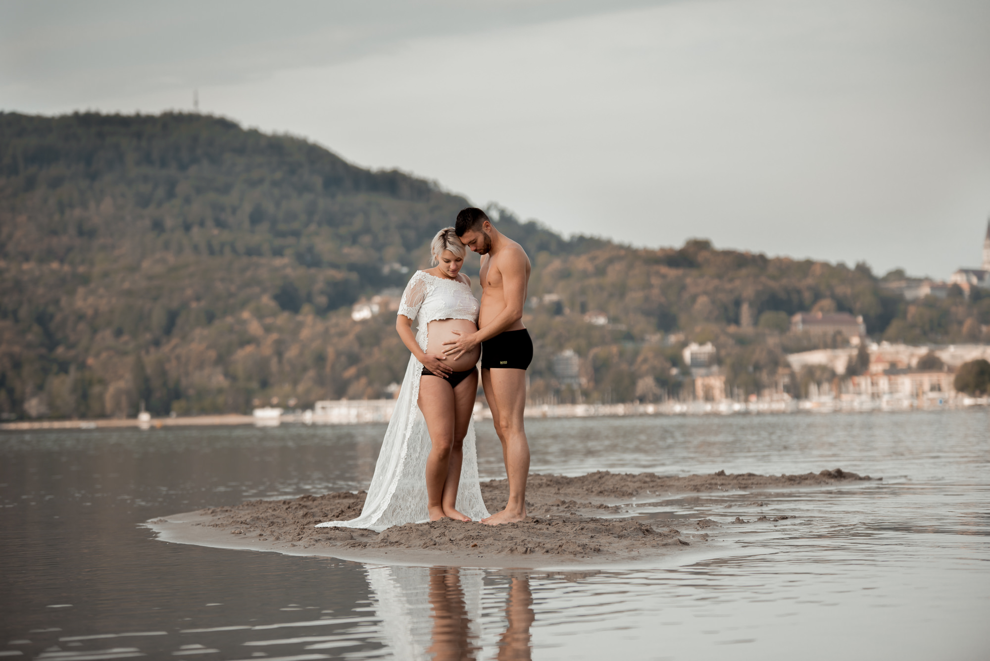 couple caressant le ventre de la maman enceinte au milieu du lac d'Annecy vêtue d'une robe blanche en dentelles